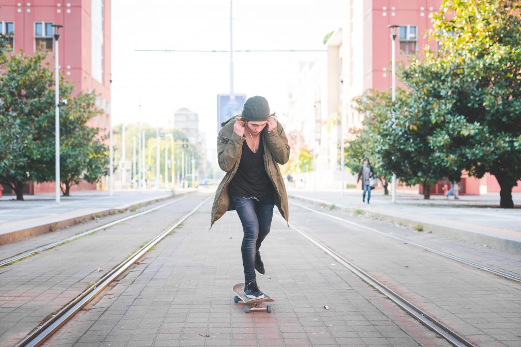 Jeune homme avec des écouteurs qui roule sur un skateboard dans la rue